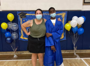 Graduating student and faculty member posing for picture infront of balloons and banner