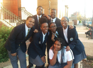 St Malachy students posing for a picture in school uniforms outside of school on the sidewalk
